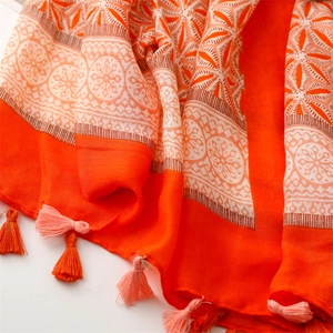 Detailed view of orange cotton linen scarf with white floral patterns and soft fringe