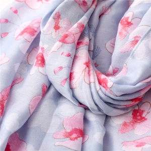 Close-up of light blue cotton linen scarf with pink floral pattern and soft woven texture