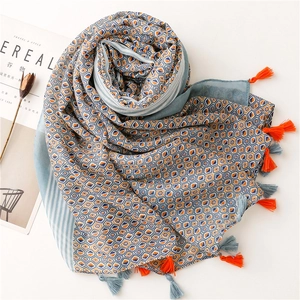 Detail of blue and orange geometric scarf with fringe tassels and soft floral props