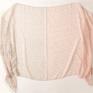 Détail d'une écharpe fleurie avec des pompons orange et un tissu bicolore pastel