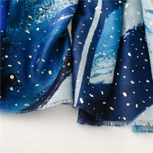 Detail of blue gradient cotton scarf featuring gold foil star pattern and frayed edges