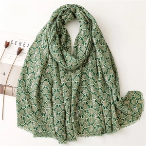 Detail of green scarf with white tree patterns and delicate fringe borders on flat lay