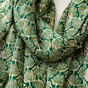 Close-up of soft green cotton scarf with elegant golden leaf pattern and textured fringe