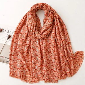 Elegant orange and beige leaf print scarf with fringe edges laid on a white surface
