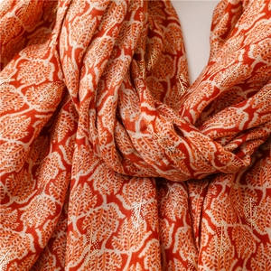 Detailed close-up of orange scarf with white leaf prints and gold foil leaf veins