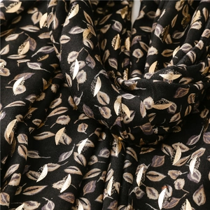 Close-up of black scarf featuring metallic gold leaf patterns and soft woven texture