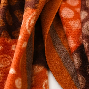 Detailed close-up of warm orange paisley dot patterns on soft cashmere feel knit fabric