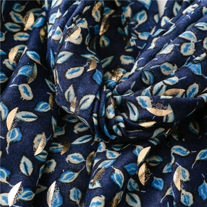 Detail of dark blue scarf featuring gold foil leaf patterns and soft woven texture