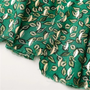 Macro detail of dark green scarf fabric with golden leaf pattern and textured fringe
