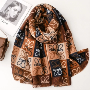 Detail of soft cashmere-feel scarf featuring orange and navy geometric patterns and fringes