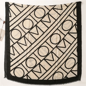 Detail of soft beige cotton scarf with black geometric letter patterns and frayed edges