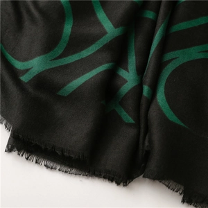 Close-up of black scarf fabric with green abstract patterns and soft fringe detailing
