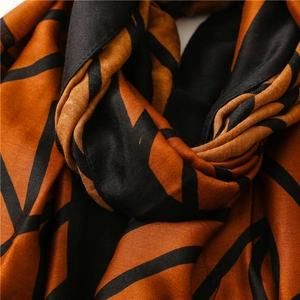 Detailed view of soft orange and black silk-feel scarf with abstract geometric lines