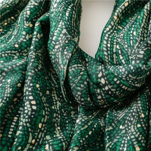 Détail d'une écharpe verte à pois dorés montrant la texture douce du tissu de qualité