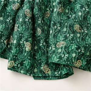 Macro shot of dark green scarf fabric with golden paisley patterns and soft texture