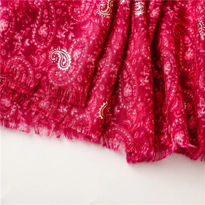 Detail of red paisley scarf featuring gold foil patterns and delicate fringed edges
