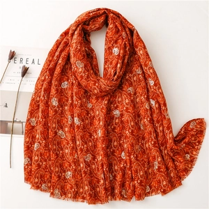Detail of red paisley scarf with gold stamping and delicate fringed edges on fabric