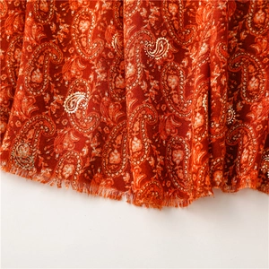 Detailed macro view of red paisley fabric featuring golden foil print and frayed edges