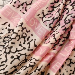 Macro detail of lightweight pink scarf fabric featuring black spots and white LOVE print