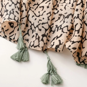 Detailed view of beige leopard print scarf with sage green tassels and woven linen texture