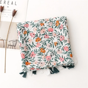 Detail of floral printed scarf with pink flowers and green tassel fringe on linen fabric