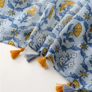 Detailed close-up of light blue scarf with yellow floral prints and bicolor fringe tassels