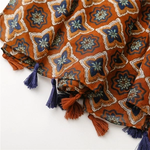 Macro detail of ethnic floral cotton scarf featuring decorative orange and navy tassels