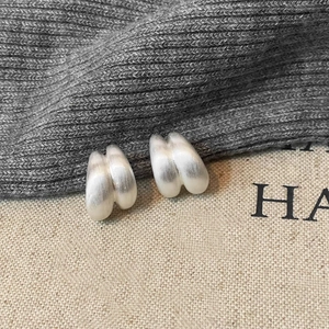 Detail of matte silver brushed earrings with thick double-row wavy design on knit fabric