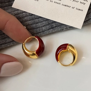 Detail view of gold U-shaped earrings with red enamel glaze and luxury minimalist finish