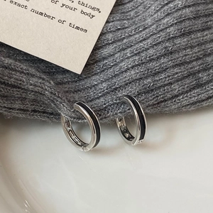 Close-up of silver-tone hoop earrings with black enamel stripes on grey knit fabric