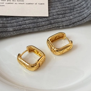 Square gold hoop earrings featuring a quilted pattern on a white porcelain plate