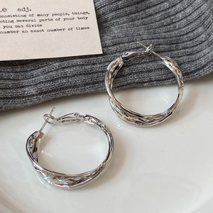 Dettaglio di orecchini a cerchio in argento con trama intrecciata su maglia grigia