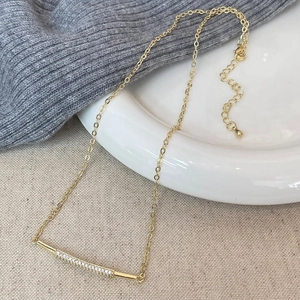 Close-up of a gold bar necklace with micro-paved zircons on elegant textured fabric