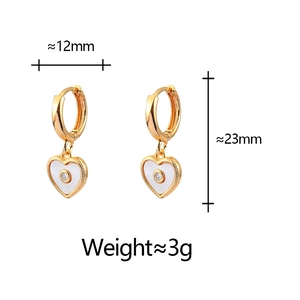 Detail view of heart-shaped gold earrings with white shell inlay and zircon stone