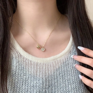 Gold heart pendant necklace with S-letter charm worn by a model on a simple background