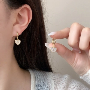Elegant gold heart earrings with white inlay and center crystal on a female model