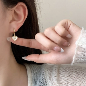 Close-up of golden heart earrings with white mother of pearl inlay and small zircon stone