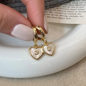 Detailed macro view of heart-shaped gold earrings with shell inlay and clear zircon stone