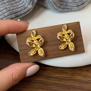 Detailed close-up of golden abstract flower earrings on a textured wooden card holder