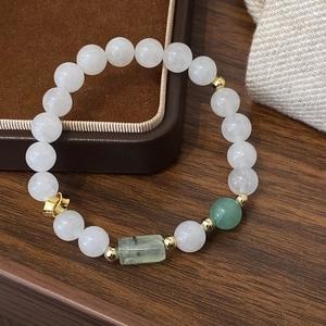 Elegant white jade bead bracelet with green stone and gold accents on a wood surface