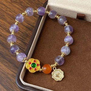 Bracelet en améthyste avec pendentif fleur dorée posé sur un écrin en cuir brun