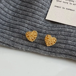 Elegant gold hollow mesh heart stud earrings displayed on a minimalist grey knit background