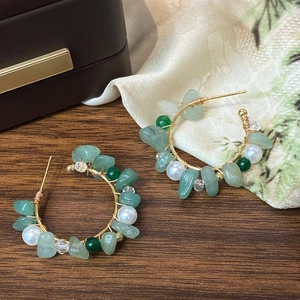 Detail of bohemian hoop earrings with green natural stones, pearls and gold wire wrap