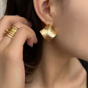 Detail of golden geometric square earrings with textured finish worn by a model