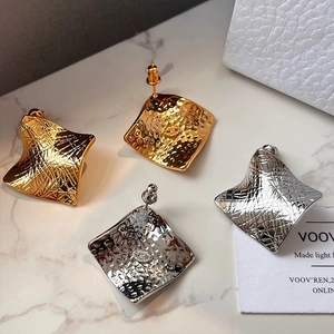 Close-up of square hammered metal earrings in gold and silver on marble background