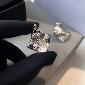 Macro close-up of geometric square earrings with hammered texture in bright silver finish