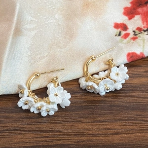 Close-up of golden semi-hoop earrings featuring five delicate white resin flower petals