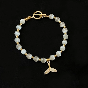 Cat eye stone beaded bracelet with fishtail charm and golden toggle clasp on black velvet