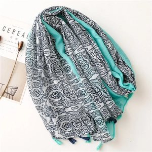 Bohemian style oversized scarf with teal ethnic prints and decorative fringes on white surface