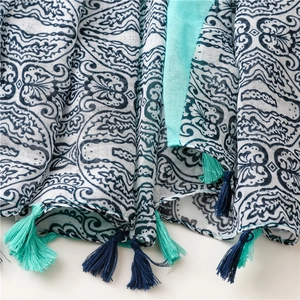 Detail of white scarf featuring blue paisley patterns and soft tassels on the edges